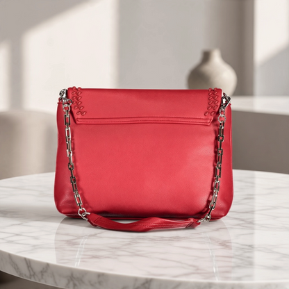 Bolso Byblos de liquidationlive en color rojo con solapa, detalle trenzado y cadena plateada sobre mesa de mármol