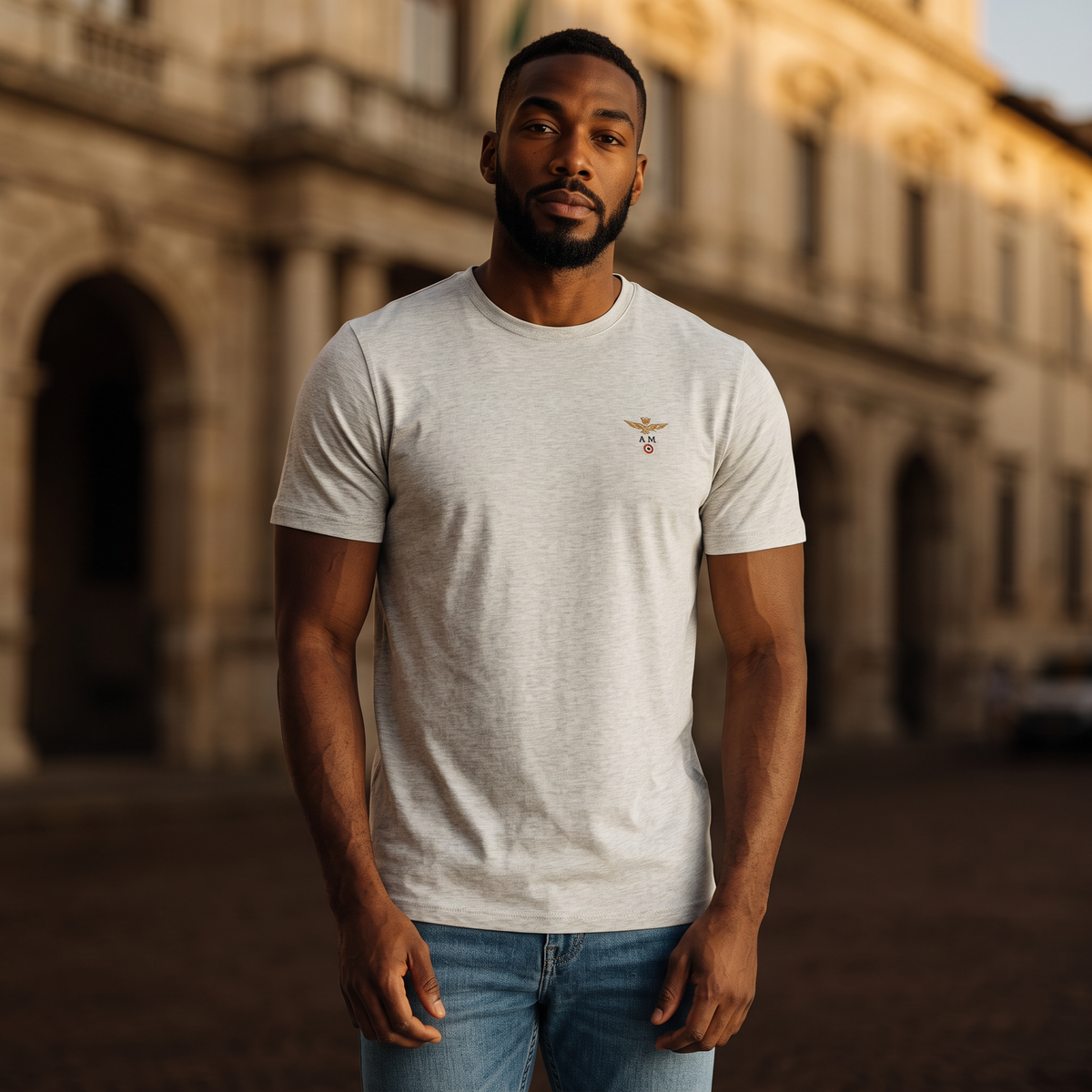 Hombre con camiseta gris de cuello redondo Aeronautica Militare con logo de alas en el pecho en entorno urbano