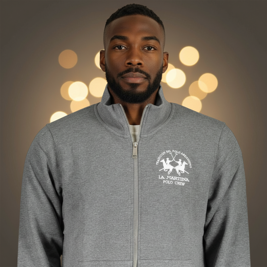Hombre vistiendo sudadera gris con cremallera y bordado de La Martina liquidationlive sobre fondo con luces bokeh