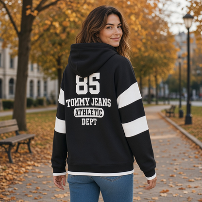 Mujer vistiendo sudadera negra con capucha Tommy Hilfiger con estampado deportivo blanco en un parque otoñal